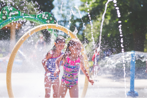 Two young girls standing among spraying water in bathing suits