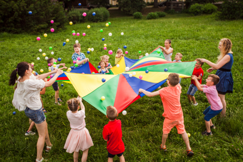 A couple of children and parents playing with a colorful parachute and many colorful balls