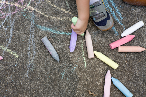 A picture of a driveway with chalk drawings and pieces of chalk