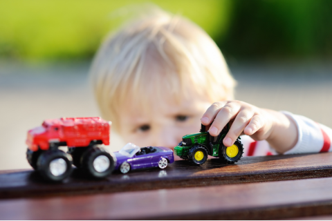 A young boy plays with 3 little toy cars