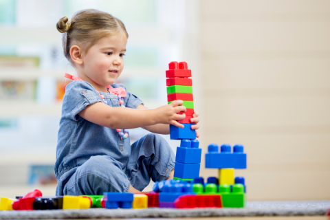 A young girl plays with colorful large building box on the floor.