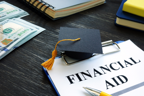 A dark table with paper that says Financial Aid. There is also a small graduation cap and some school items.