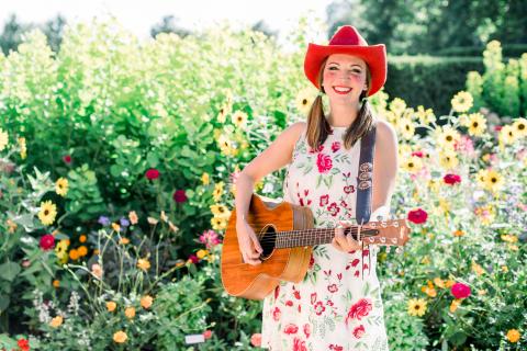 Miss Jamie holding a guitar in a park.