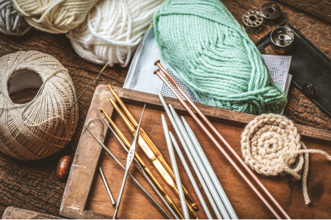 On a table there is an assortment of knitting and crochet supplies including yarn, hooks, and needles.