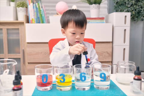 A toddler prepares to drop blue dye into a large clear container