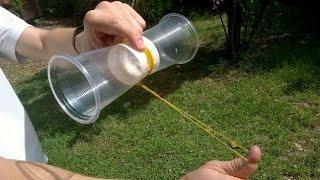 A man pulls on rubber band on a magnus glider made with tape and two clear cups