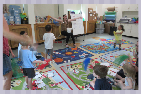A librarian singing a song with scarves with a group of kids and adults.