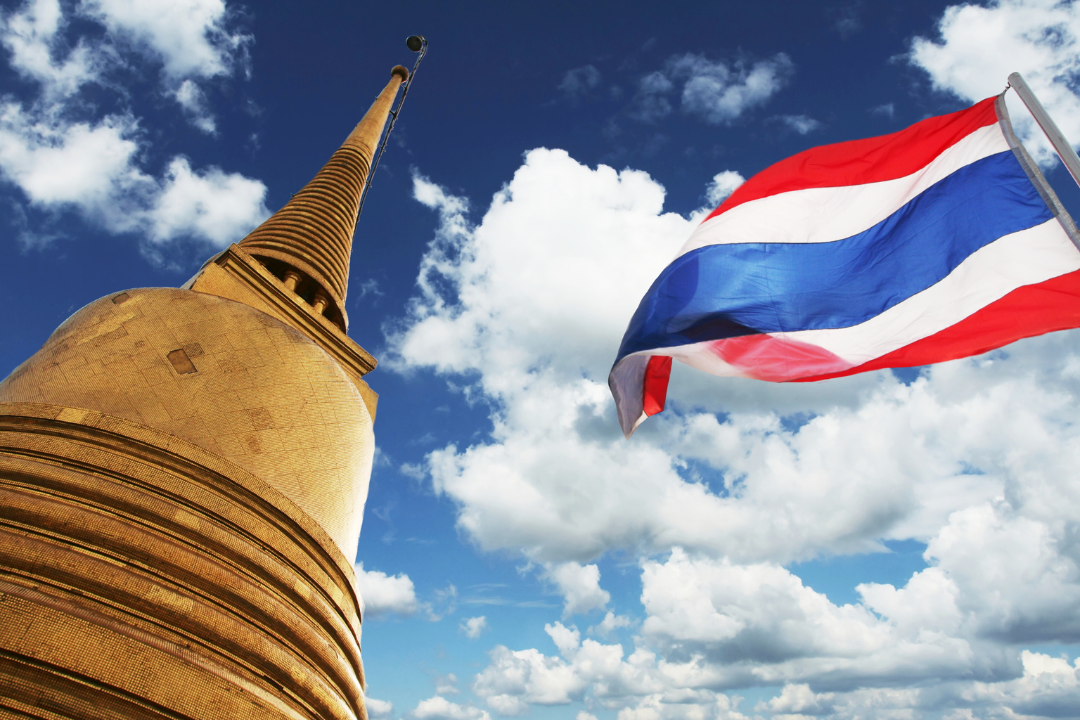 A Thailand flag waving next to a tall building