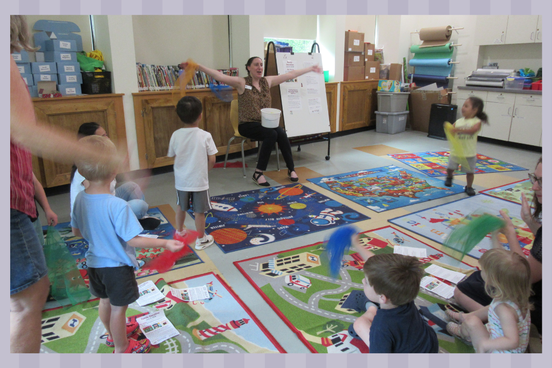 A teacher singing a song with scarves with a group of kids and adults.